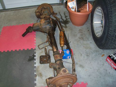 1978 Jeep CJ5 - A rusty front axle assembly, likely from an older vehicle, sits on a tiled garage floor next to a tire.