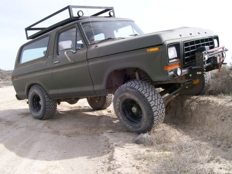 1979 Ford Bronco - This modified Ford Bronco is navigating an off-road trail with its front tires on an elevated dirt mound.