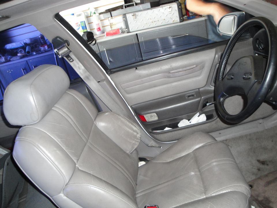 Car interior with gray leather seats, door panel, and steering wheel. A person's arm is visible near the window