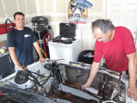 1989 Ford Taurus - Two men are actively working on the engine bay of a car, suggesting a repair or modification is in progress.