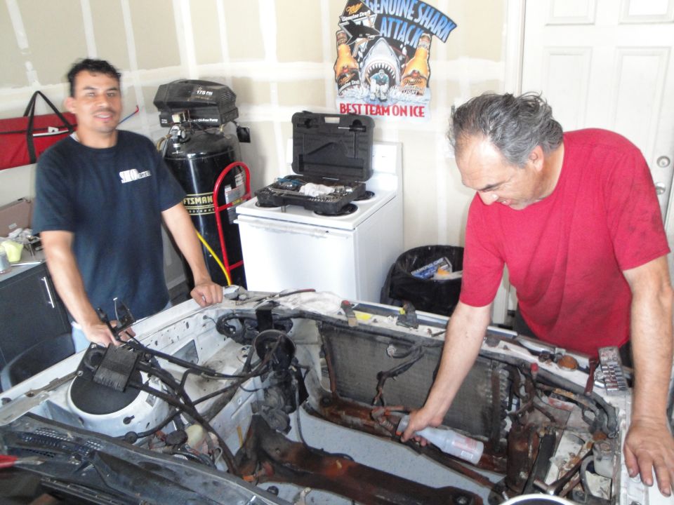 Two men working on a car's engine bay, which is open and appears to be undergoing maintenance or an engine swap