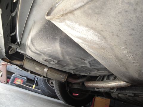 1989 Ford Taurus - The underside of a vehicle reveals the fuel tank and exhaust components, with some part numbers visible on the tank.