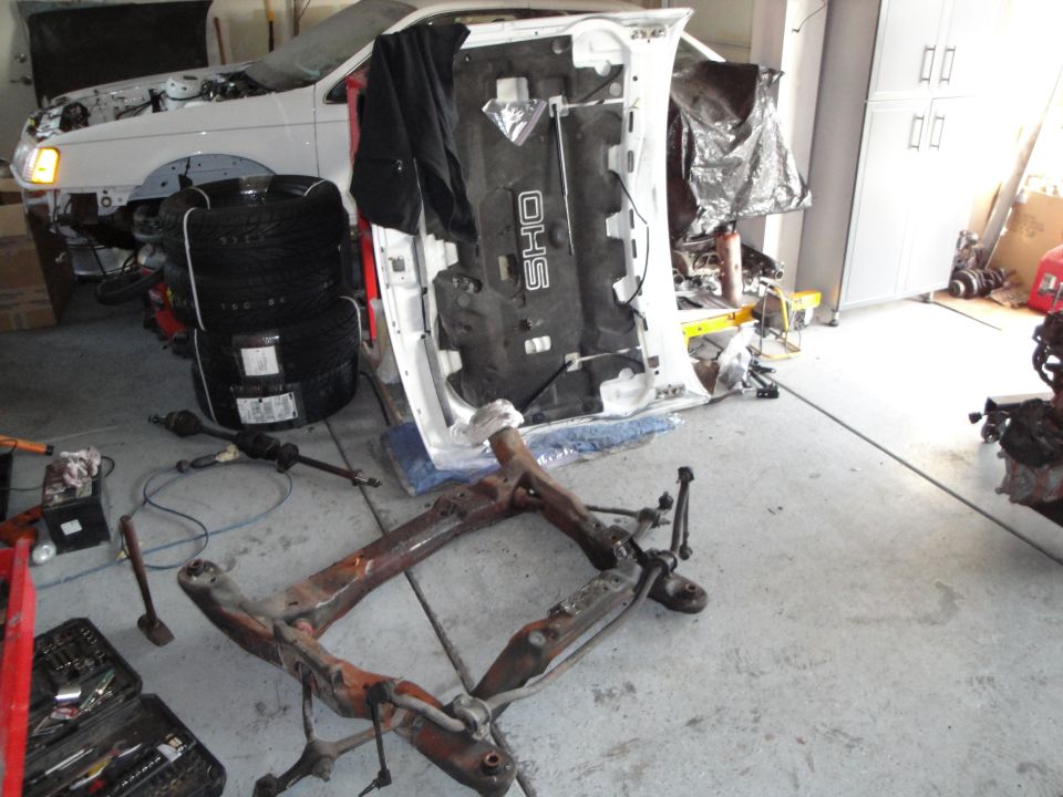 Disassembled 1989 Ford Taurus engine bay with SHO hood liner, tires, and subframe on floor