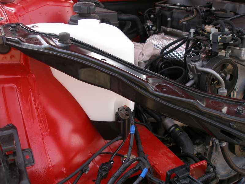 Engine bay showing a white plastic coolant reservoir and engine components. Red painted metal is visible