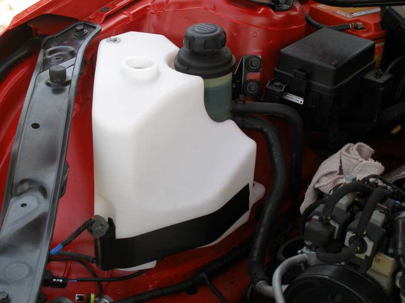 2010 Hyundai Genesis windshield washer fluid reservoir and engine components under red hood