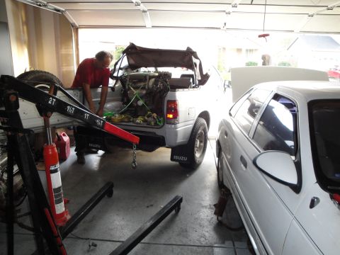 1989 Ford Taurus - An engine is being removed from a silver Isuzu pickup truck with a hoist in a garage, next to a white sedan.