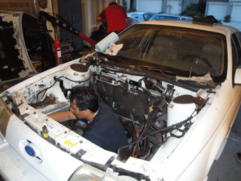 1989 Ford Taurus - Mechanic works on a white 1989 Ford Taurus as the engine is being removed or installed.
