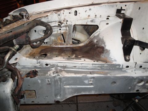 1989 Ford Taurus - The engine bay of a white car shows exposed wiring, rust, and a mounting bracket.
