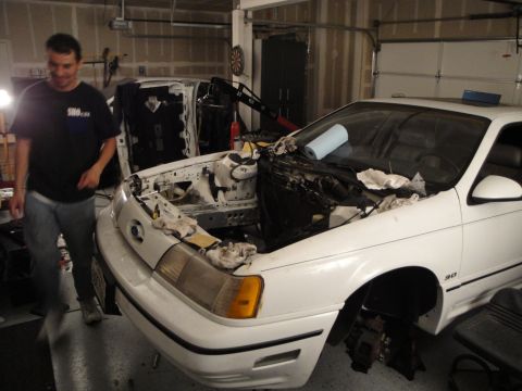 1989 Ford Taurus - A white 1989 Ford Taurus is in a garage with its engine removed, undergoing maintenance.