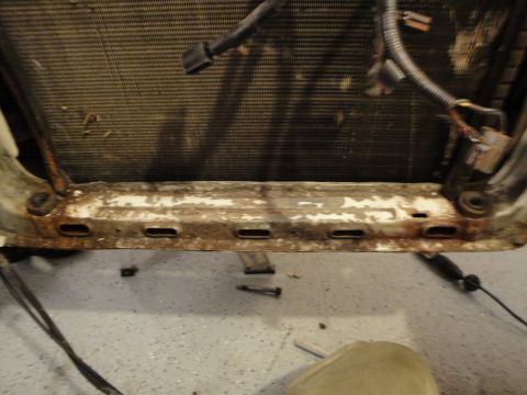 1989 Ford Taurus - Close-up of a vehicle's radiator and its corroded mounting bracket, with visible wiring.