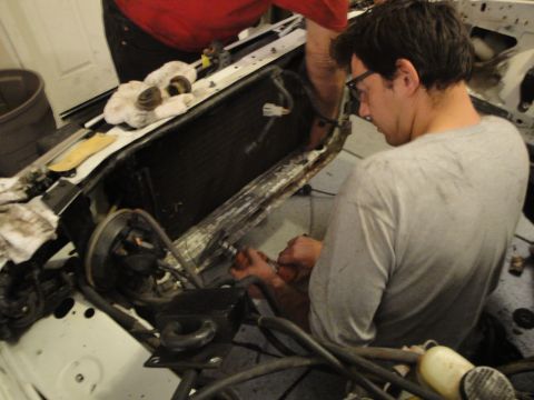 1989 Ford Taurus - Mechanic works on the engine bay of a car, with the radiator removed and various hoses and wires exposed.