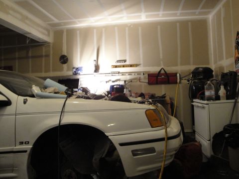 1989 Ford Taurus - A white sedan is parked in a garage, with its hood open and various tools and equipment visible in the background.