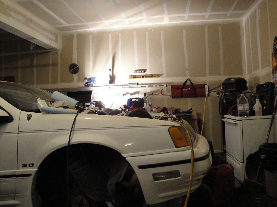 White sedan with hood open, parked in a garage with tools on the wall
