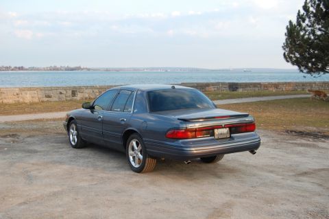 1985 Mercury Grand Marquis - A Mercury Grand Marquis is parked near a body of water with a stone wall in the background.