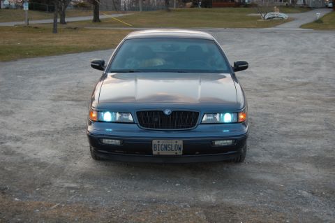 1985 Mercury Grand Marquis - This dark blue sedan features a prominent black grille and a custom license plate. The body style suggests a model from the late 1990s or e…