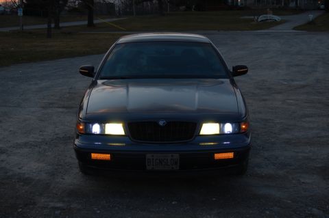 1985 Mercury Grand Marquis - The front of a Mercury Grand Marquis is shown at dusk, with its headlights and amber marker lights illuminated.