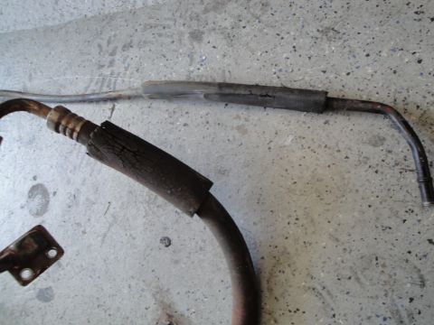 1989 Ford Taurus - Close-up of a worn engine part, possibly a hose or pipe, showing significant cracking in its protective insulation against a concrete backg…