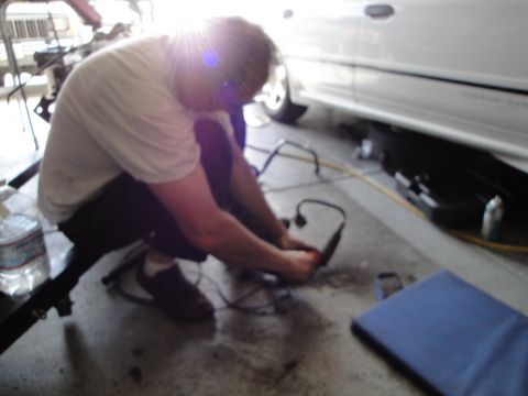 1989 Ford Taurus - A person crouches down to work on the wiring of a white vehicle.