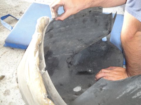 1989 Ford Taurus - A person is holding a damaged black plastic car fender liner, which is partially wrapped in protective material.