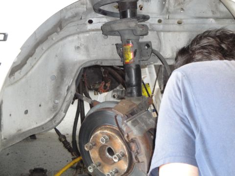 1989 Ford Taurus - Close-up view of a car's front suspension and brake assembly, with a person partially visible.
