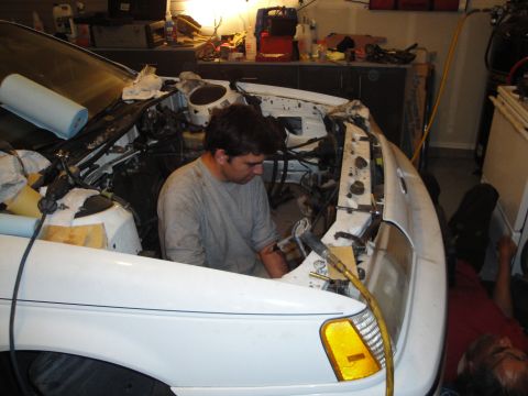 1989 Ford Taurus - Mechanics work on a car's engine bay in a cluttered garage setting.