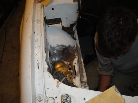 1989 Ford Taurus - A person works on the engine bay of a white car, showing signs of rust and repair.