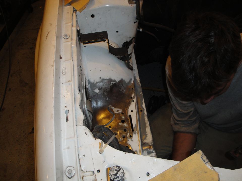 White car engine bay with rust and exposed metal, a person works on it
