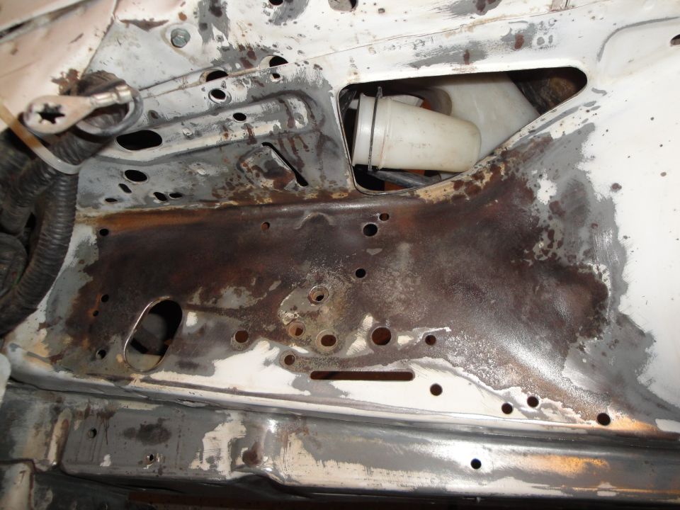 Engine bay with significant rust and damage, showing a white plastic reservoir