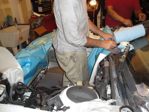 1989 Ford Taurus - Two people are working on a car's engine bay, with tools and parts visible.