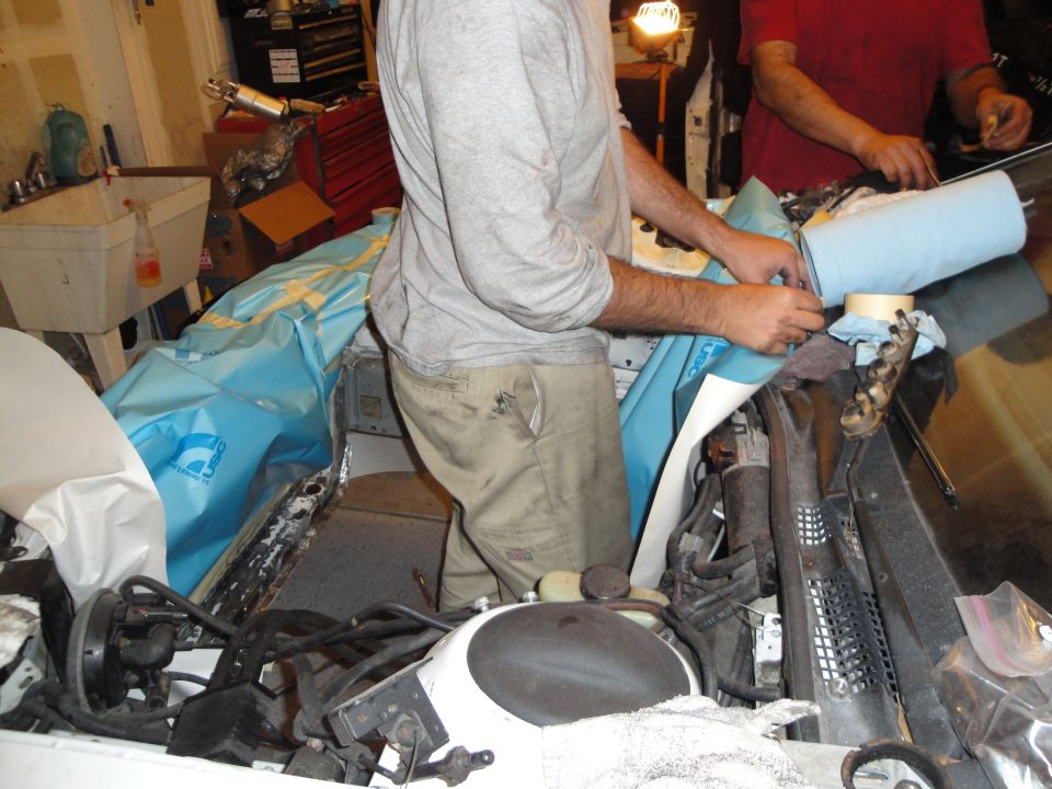 Mechanics working on an engine bay, with blue tarp covering parts