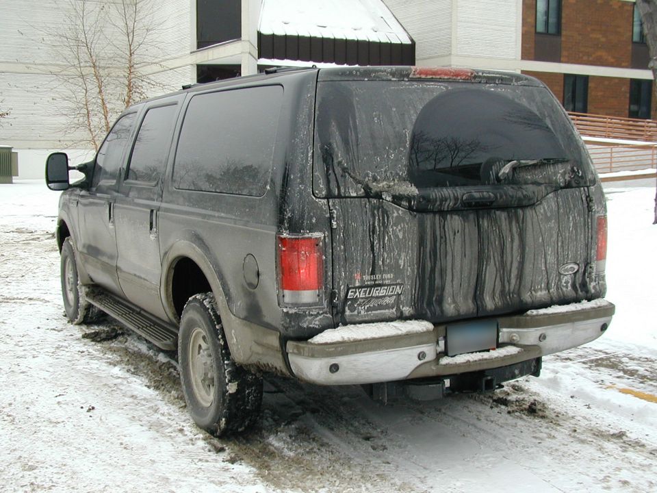 Muddy black Ford Excursion SUV parked in snow, rear three-quarter view