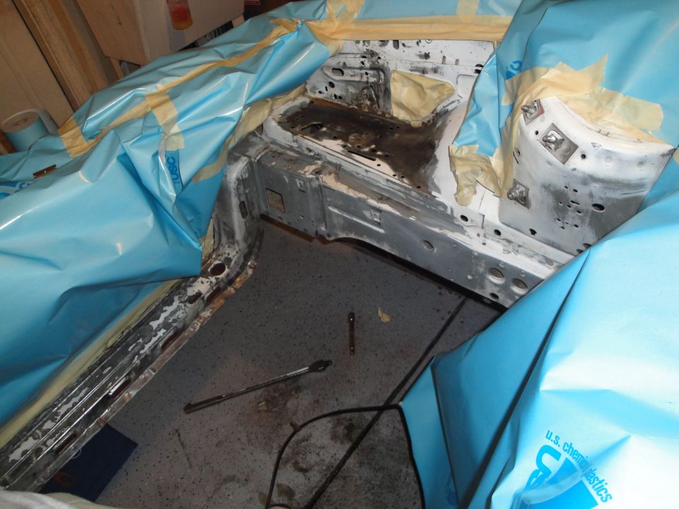 Car interior stripped down, covered in blue plastic sheeting and masking tape, with tools on the floor