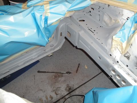 1989 Ford Taurus - The bare frame of a car is visible, covered in protective sheeting and masking tape, with tools scattered on the floor.