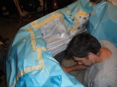 1989 Ford Taurus - A person works on a vehicle's engine bay, which is covered in protective sheeting.