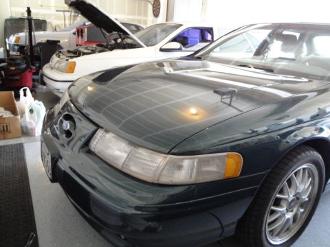 1989 Ford Taurus - Two cars in a garage, one dark green and one white with its hood up.