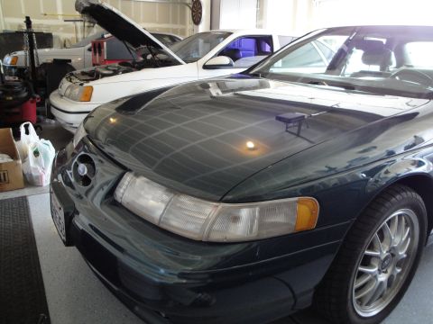 1989 Ford Taurus - Two Ford Tauruses are parked in a garage, one with its hood open.