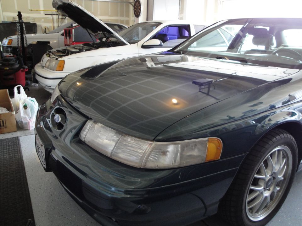 Dark green Ford Taurus in garage, white Taurus with hood up behind it