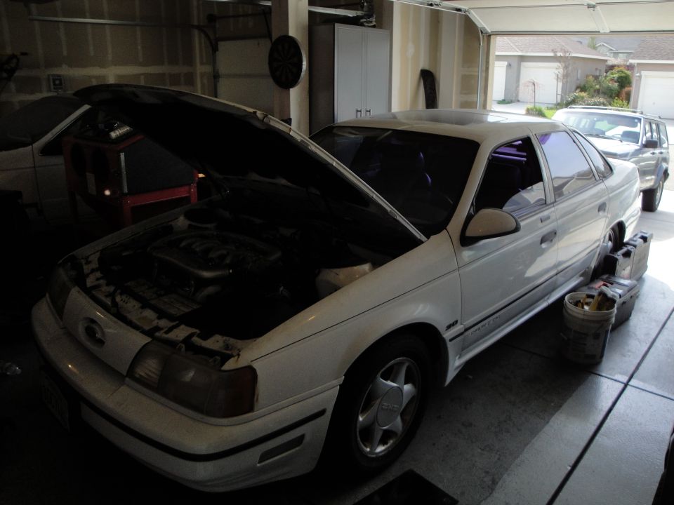 White 1989 Ford Taurus with hood open, engine visible, parked in garage