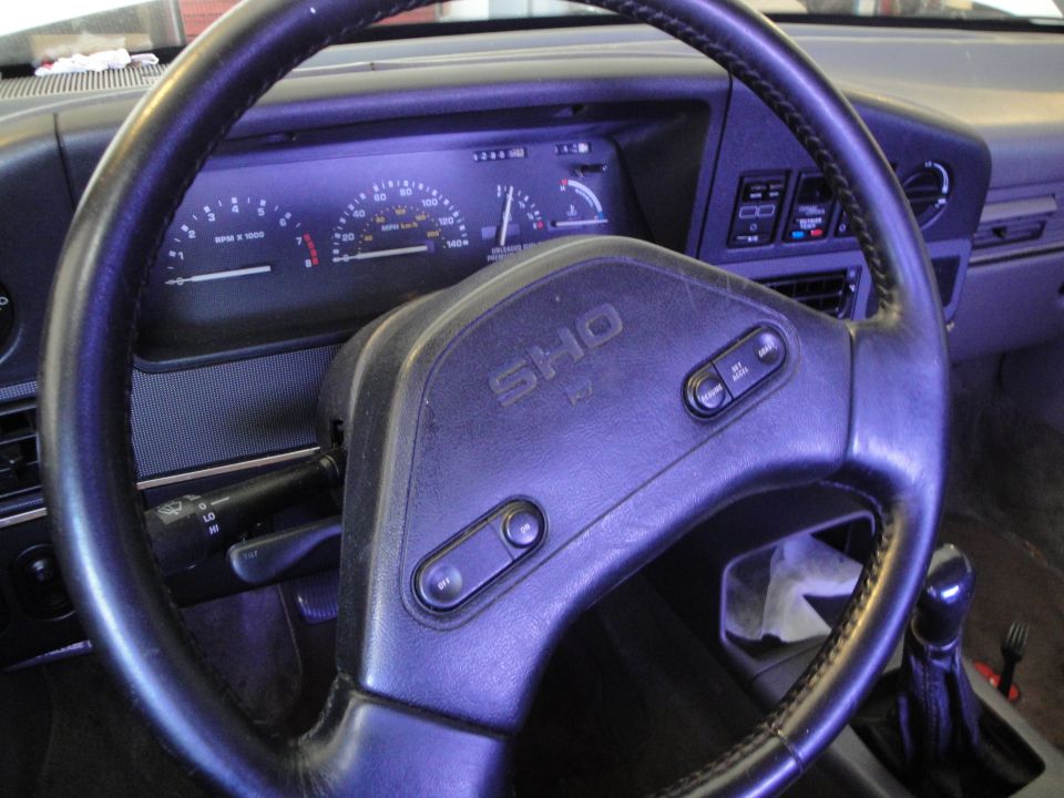 Interior view of a car's steering wheel with 'SHO' emblem and dashboard gauges