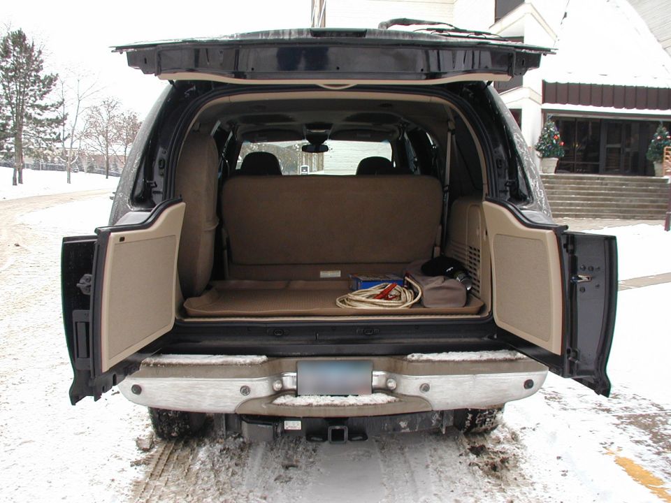 Rear of black SUV with open tailgate doors showing tan cargo area, parked in snow