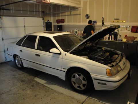 1989 Ford Taurus - White 1989 Ford Taurus with its hood open in a garage setting.