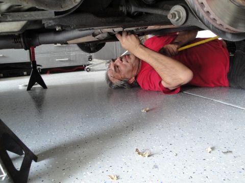 1989 Ford Taurus - A person works on the undercarriage of a vehicle that is raised on jack stands in a garage.