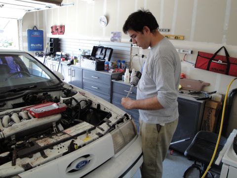 1989 Ford Taurus - Man works on the engine of a white Ford sedan in a garage.