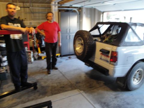 1989 Ford Taurus - Two men in a garage stand near a white convertible SUV that has a spare tire on its rear.