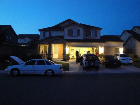 1989 Ford Taurus - A white 1989 Ford Taurus sedan sits in front of a house with its hood open, alongside other vehicles.