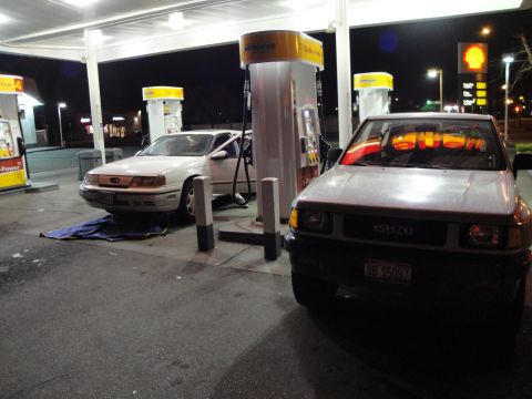 1989 Ford Taurus - Two vehicles are parked at gas pumps under a Shell station canopy at night.