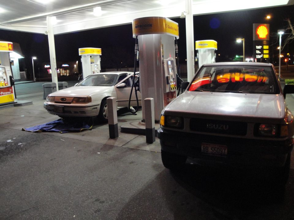 white sedan and gray SUV at gas pumps at night
