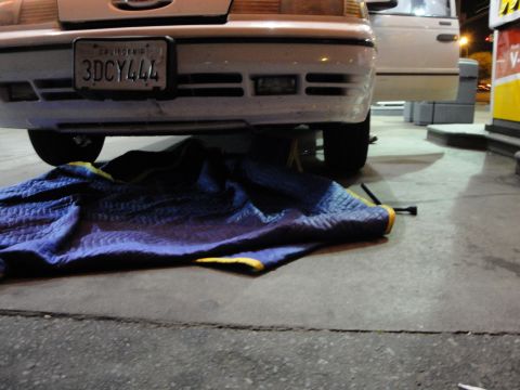1989 Ford Taurus - A white 1992 Ford Crown Victoria is seen from the rear, elevated by a jack with a blue blanket spread below.
