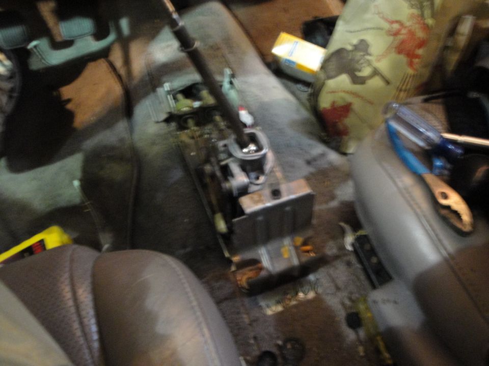 Disassembled center console with shift lever mechanism exposed, tools on seats