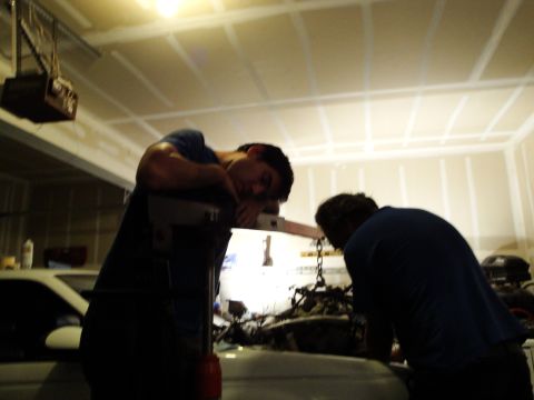 1989 Ford Taurus - Garage scene with two individuals attending to an engine, possibly during a swap or repair.
